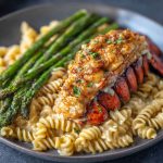 Succulent Cajun butter lobster tail served over creamy garlic pasta with roasted asparagus, garnished with fresh herbs.