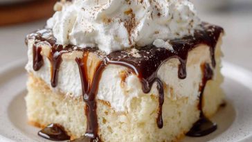White Russian poke cake infused with coffee liqueur and vodka, topped with creamy whipped frosting and chocolate drizzle.