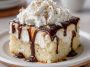 White Russian poke cake infused with coffee liqueur and vodka, topped with creamy whipped frosting and chocolate drizzle.