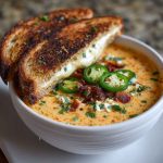 Bowl of spicy jalapeño popper soup with grilled cheese dippers on the side