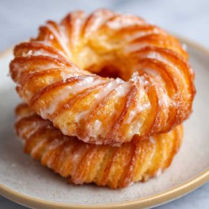 Golden oven-baked French cruller donuts with a light, airy texture, drizzled with sweet glaze and served on a tray.