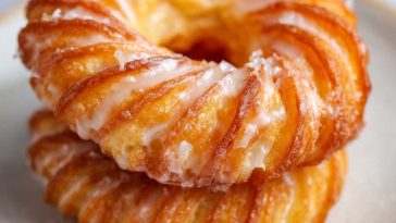 Golden oven-baked French cruller donuts with a light, airy texture, drizzled with sweet glaze and served on a tray.