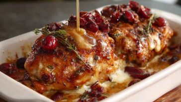 Golden baked chicken topped with honey cranberry glaze and creamy ricotta cheese, served in a casserole dish.