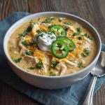 Creamy white cheddar apple chicken chili served in a rustic bowl, topped with shredded cheese and fresh herbs.