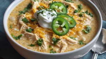 Creamy white cheddar apple chicken chili served in a rustic bowl, topped with shredded cheese and fresh herbs.