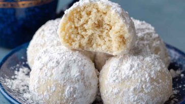 Sweetened condensed milk snowball cookies dusted with powdered sugar, stacked on a festive holiday plate.