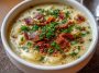 Bowl of creamy garlic potato soup garnished with fresh herbs and crusty bread on the side.