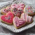 Homemade Valentines cookies decorated with pink and red icing, heart-shaped sprinkles, and festive designs arranged on a platter.