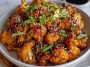 “Crispy baked cauliflower florets coated in spicy Korean-style gochujang sauce, garnished with sesame seeds and green onions.”