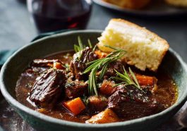 French-style beef stew with tender beef chunks, carrots, onions, and potatoes simmered in a rich red wine sauce, served in a rustic bowl.