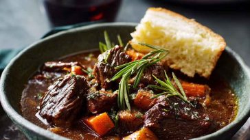 French-style beef stew with tender beef chunks, carrots, onions, and potatoes simmered in a rich red wine sauce, served in a rustic bowl.