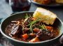 French-style beef stew with tender beef chunks, carrots, onions, and potatoes simmered in a rich red wine sauce, served in a rustic bowl.