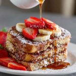 A golden-brown overnight French toast casserole topped with powdered sugar and fresh berries, served on a rustic plate.