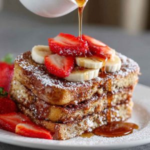 A golden-brown overnight French toast casserole topped with powdered sugar and fresh berries, served on a rustic plate.