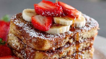 A golden-brown overnight French toast casserole topped with powdered sugar and fresh berries, served on a rustic plate.