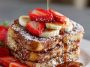 A golden-brown overnight French toast casserole topped with powdered sugar and fresh berries, served on a rustic plate.