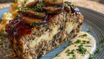 Sliced mushroom Swiss cheese meatloaf topped with melted cheese and fresh herbs.
