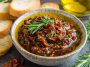 “A rustic bowl of Mediterranean sun dried tomato garlic olive oil dip served with crusty bread and fresh herbs.”