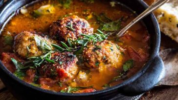 “A hearty bowl of Italian meatball soup with tender meatballs, pasta, vegetables, and fresh herbs served with bread.”