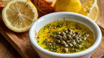 "A small dish of simple lemon caper sauce with fresh lemon slices and capers, served alongside grilled fish."