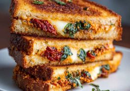 Golden grilled cheese sandwich filled with melted mozzarella, sun-dried tomato pesto, and fresh basil leaves.