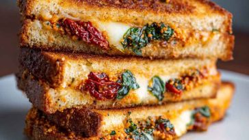 Golden grilled cheese sandwich filled with melted mozzarella, sun-dried tomato pesto, and fresh basil leaves.
