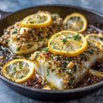 Gluten-free Mediterranean baked cod fillet with lemon slices, garlic, and fresh herbs served on a rustic platter.