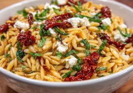 Colorful orzo pasta salad with crumbled feta, sun-dried tomatoes, fresh herbs, and a light Mediterranean dressing served in a bowl.