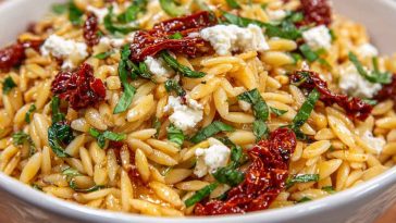 Colorful orzo pasta salad with crumbled feta, sun-dried tomatoes, fresh herbs, and a light Mediterranean dressing served in a bowl.