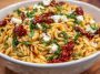Colorful orzo pasta salad with crumbled feta, sun-dried tomatoes, fresh herbs, and a light Mediterranean dressing served in a bowl.