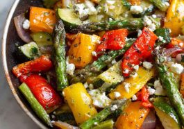 A colorful one-pan dish of roasted Greek vegetables including zucchini, bell peppers, tomatoes, onions, and potatoes, drizzled with olive oil and herbs.