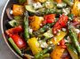A colorful one-pan dish of roasted Greek vegetables including zucchini, bell peppers, tomatoes, onions, and potatoes, drizzled with olive oil and herbs.