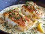 "Golden pan-seared cod fillets topped with creamy garlic sauce, served with fresh herbs and lemon wedges."