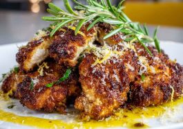 “Golden crispy lemon pecorino chicken served on a plate with fresh herbs and lemon wedges.”