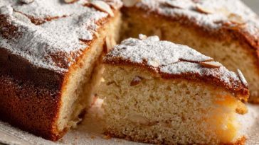 “A golden Italian torta della nonna topped with pine nuts and powdered sugar, sliced to reveal creamy custard filling.”
