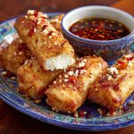 Golden oven-fried feta rolls drizzled with spicy chili honey, crispy appetizer with a sweet-heat kick.