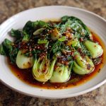 Stir-fried bok choy drizzled with ginger chili sauce and garnished with sesame seeds.