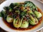 Stir-fried bok choy drizzled with ginger chili sauce and garnished with sesame seeds.