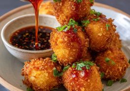 A plate of golden-brown crispy shrimp balls served with a side of sweet chili dipping sauce, garnished with fresh herbs.