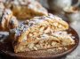 “A golden, flaky almond kringle pastry drizzled with icing and sprinkled with sliced almonds, served on a rustic platter.”