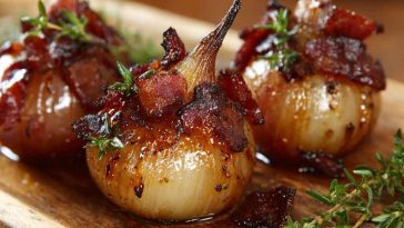 Honey-glazed shallots topped with crispy bacon pieces served in a rustic dish.