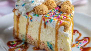 Slice of sugar cookie cheesecake topped with whipped cream and colorful sprinkles.