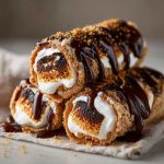 Golden s’mores roll-ups filled with gooey marshmallows, melted chocolate, and graham cracker crumbs, served warm on a plate.
