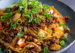“A skillet filled with Mongolian ground beef and cabbage stir-fry, garnished with sesame seeds and green onions.”