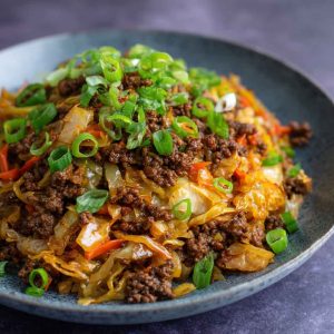 “A skillet filled with Mongolian ground beef and cabbage stir-fry, garnished with sesame seeds and green onions.”