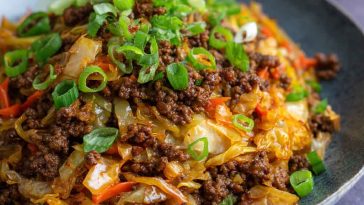 “A skillet filled with Mongolian ground beef and cabbage stir-fry, garnished with sesame seeds and green onions.”