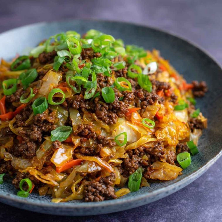 “A skillet filled with Mongolian ground beef and cabbage stir-fry, garnished with sesame seeds and green onions.”