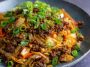 “A skillet filled with Mongolian ground beef and cabbage stir-fry, garnished with sesame seeds and green onions.”