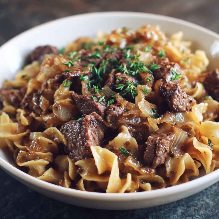 French onion beef and noodles with tender beef strips, caramelized onions, and egg noodles coated in a savory, creamy sauce served in a skillet.