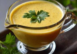 Jar of tangy mustard sauce with a spoon and fresh herbs beside it.